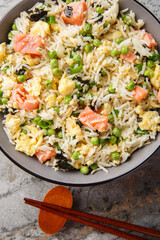 Asian fried rice with red fish, seaweed, green peas, onion and omelet close-up in a bowl on the table. Vertical top view from above