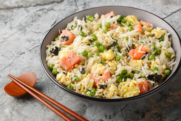 Asian food fried rice with salmon, seaweed, green peas, onion and egg close-up in bowl on table. Horizontal
