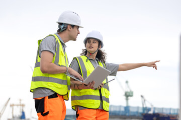 Dock Workers in Safety Uniforms Using Technology for Port Operations, Maritime Safety Engineer Working at Harbor Site, Industrial Engineers Collaborating at Port Terminal with Laptop and Walkie-Talkie