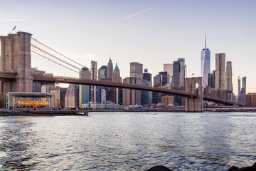 A panoramic sunset view of the Brooklyn Bridge stretching towards Manhattan