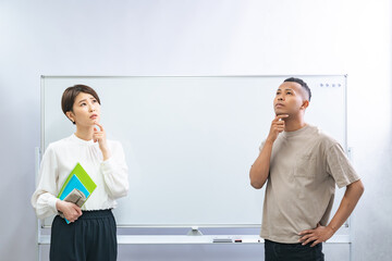 A black man and a Japanese woman thinking in front of a whiteboard in a classroom