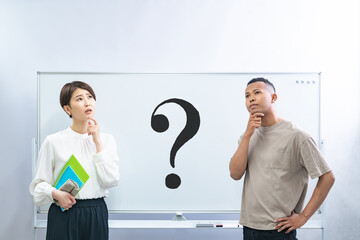 ハテナの書かれたホワイトボードの前で考える黒人男性と日本人女性