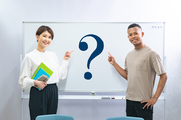 ハテナの書かれたホワイトボードを指さす黒人男性と日本人女性