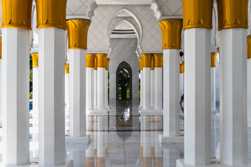 Corridor view of a building with white columns and golden tops, leading to an arched entrance with...