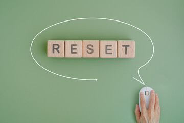 RESET text on wooden cube blocks inside speech bubble line with hand and computer mouse on green background