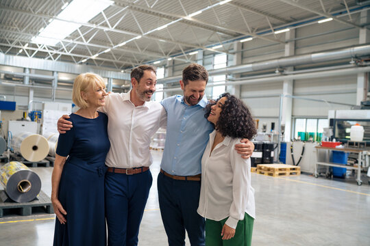 Happy business colleagues standing with arms around each other at factory