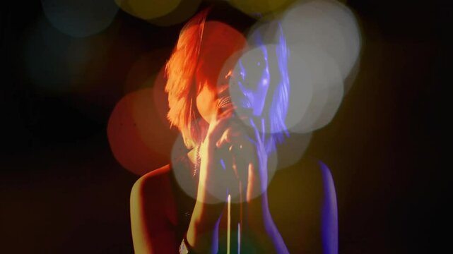 Teenage singer touching and cradling mic while facing camera illustrating music with bokeh lights