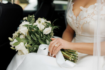 Bride holding a wedding bouquet of white flowers sitting in the car on wedding day. Close-up of the...