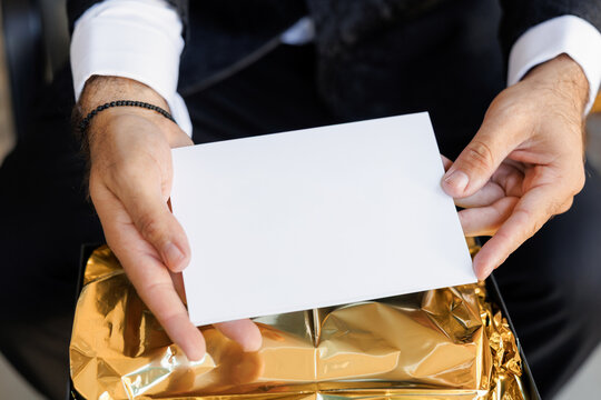 Male hands holding a sheet of paper with empty space for text close-up. Stylish man in black suit and white shirt holding a blank white paper card. Letter with copy space for text - Powered by Adobe