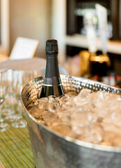 Bottle of champagne chilling in a bucket with ice cubes for celebration. Metal bucket filled with...