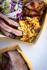 A take away container filled with smoked ribs, salad and corn bread