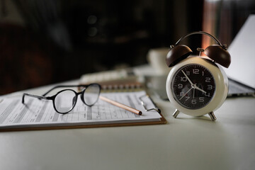 alarm clock on table near laptop, documents and eyeglasses. time management concept, routine work, education, office workplace, planning