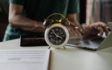 select focus on alarm clock, freelancer using laptop working in a hurry before deadline, time management concept, routine work, office hour