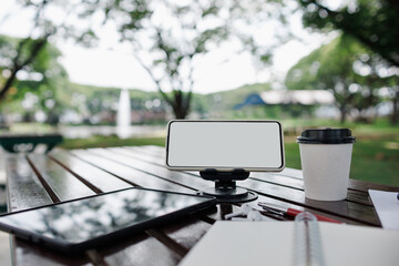 mobile phone on stand with coffee cup and tablet on wooden table in park, working outside concept and relax via modern technology from mobile