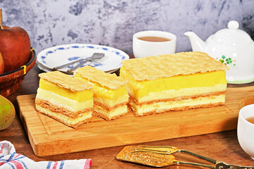 Slice of lemon napoleon cake on a wooden cutting board, selective focus