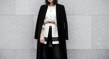 a stylish woman wearing a black coat and standing in front of a gray wall.