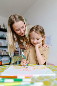 Child receiving enthusiastic feedback from sibling while drawing indoors