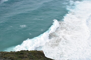 A powerful turquoise wave crashes onto the shore, captured in stunning detail from above. The...