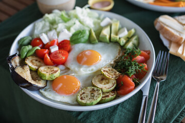 A healthy and satisfying homemade breakfast consisting of eggs, avocado, fried zucchini, eggplant, salmon, cherry tomatoes and herbs.