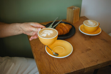 Close-up of a man sitting in a cafe drinking a cup of coffee and eating a croissant.