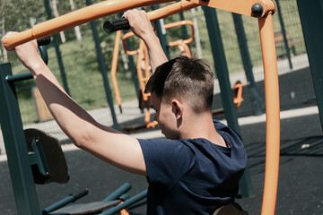 Obraz premium Young man exercising on outdoor gym equipment. Fitness workout in summer park.