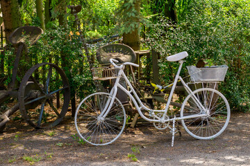 White vintage bicycle with baskets used as garden decoration among old farming tools