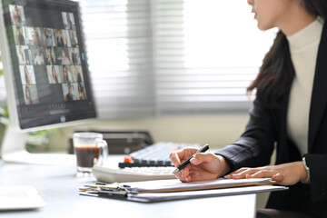 Businesswoman attending a virtual meeting, taking notes while focused on computer screen