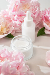 Skincare product display with cream jar, serum bottle and peony accent, ideal for e-commerce...