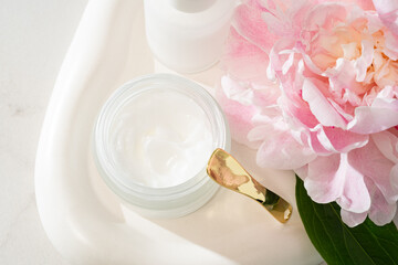 Serum dropper bottle and cream jar on a concrete tray with pink peonies. Urban-meets-natural...
