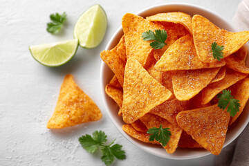 A bowl of tortilla chips with lime wedges and cilantro on top