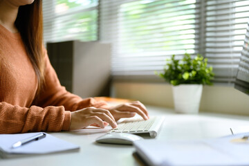 Close up of woman typing on wireless keyboard at a bright home office desk with natural light