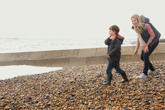 Happy mother and son skimming stones on rocky winter beach
