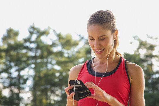 Blond female runner with headphones looking down at smart phone
