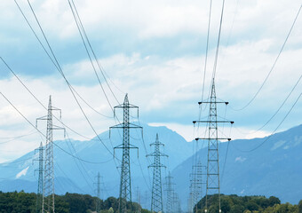 Transmission towers against mountainous backdrop on cloudy day