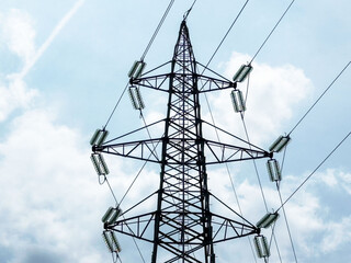 Tall metal electricity transmission tower with insulators against cloudy sky