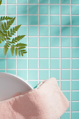 Bathroom flatlay with pink towel and green leaves over aqua tile. Simple textures and negative...