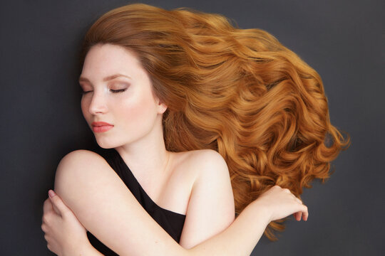 Portrait of beautiful, serene young woman with long, curly hair spread over gray background
