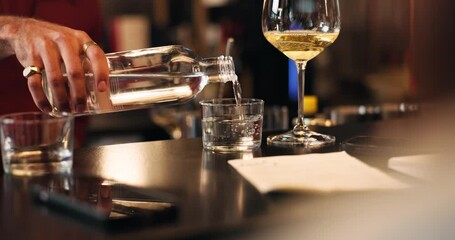 Pouring, water and wine with hand of bartender in restaurant for hospitality, refreshment or service. Alcohol, bottle and nightlife with person at counter in pub for beverage or drinks order closeup
