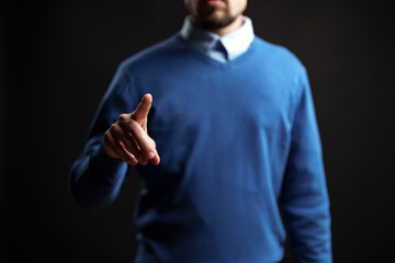 Man in blue sweater gestures confidently with a pointed finger against a dark background