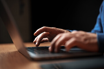 Hands typing on a laptop in a dimly lit room during the evening hours