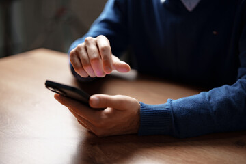 Man using smartphone while sitting at a wooden table in a cozy indoor setting during the day