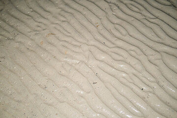 Close-up view of wet beach sand at night, showing natural ripple patterns left by the receding tide under low light