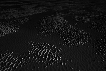 Dramatic black and white photo of beach sand ripples at night, highlighting textures and shadows from low-angle lighting