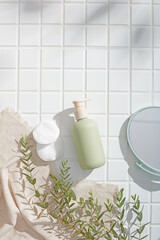 Bathroom scene with green bottle, white sponges and clear dish on square tile floor with soft...