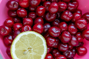 close-up of washed cherries with a lemon slice in a pink plastic bowl