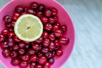 washed cherries with lemon slice in a pink plastic bowl

