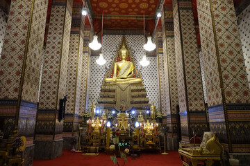 Serene interior of temple featuring large golden Buddha statue surrounded by ornate decorations and...