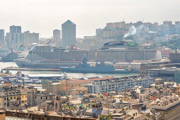Obraz premium Genoa, Italy. A large cruise ship and military vessel dock side by side in the Port of Genoa, seen above the rooftops of the historic center