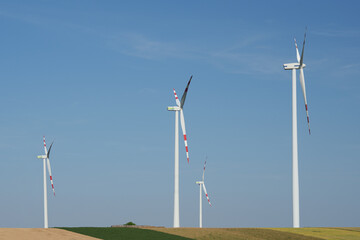 Four modern wind turbines under a clear blue sky in a field. Austria.