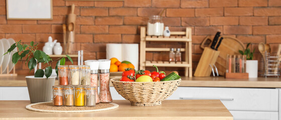 Jars with different spices, plant and vegetables on table in kitchen